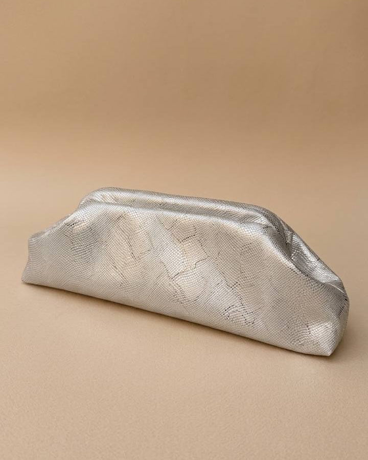 Handcrafted metallic silver vegan leather clutch bag with a textured snakeskin finish on a wooden surface.